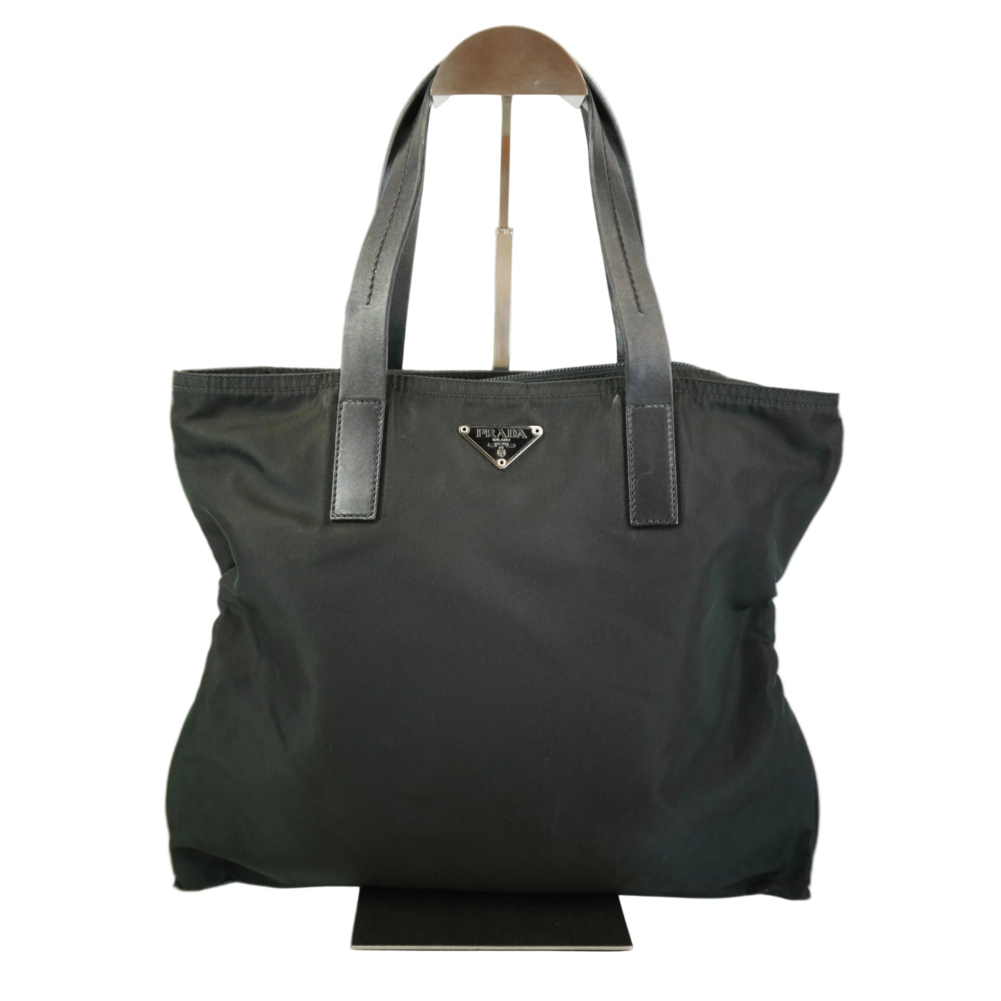 A black Prada nylon tote bag with dark gray leather shoulder straps and a silver-tone triangular logo plaque on the front, displayed on a stand against a white background.